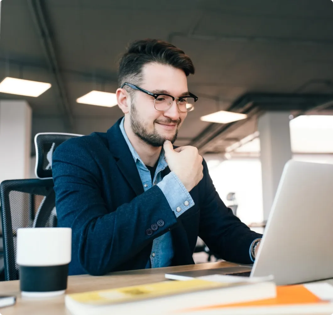 attractive-dark-haired-man-is-working-with-laptop-table-office-he-wears-blue-shirt-with-black-jacket-he-is-smiling